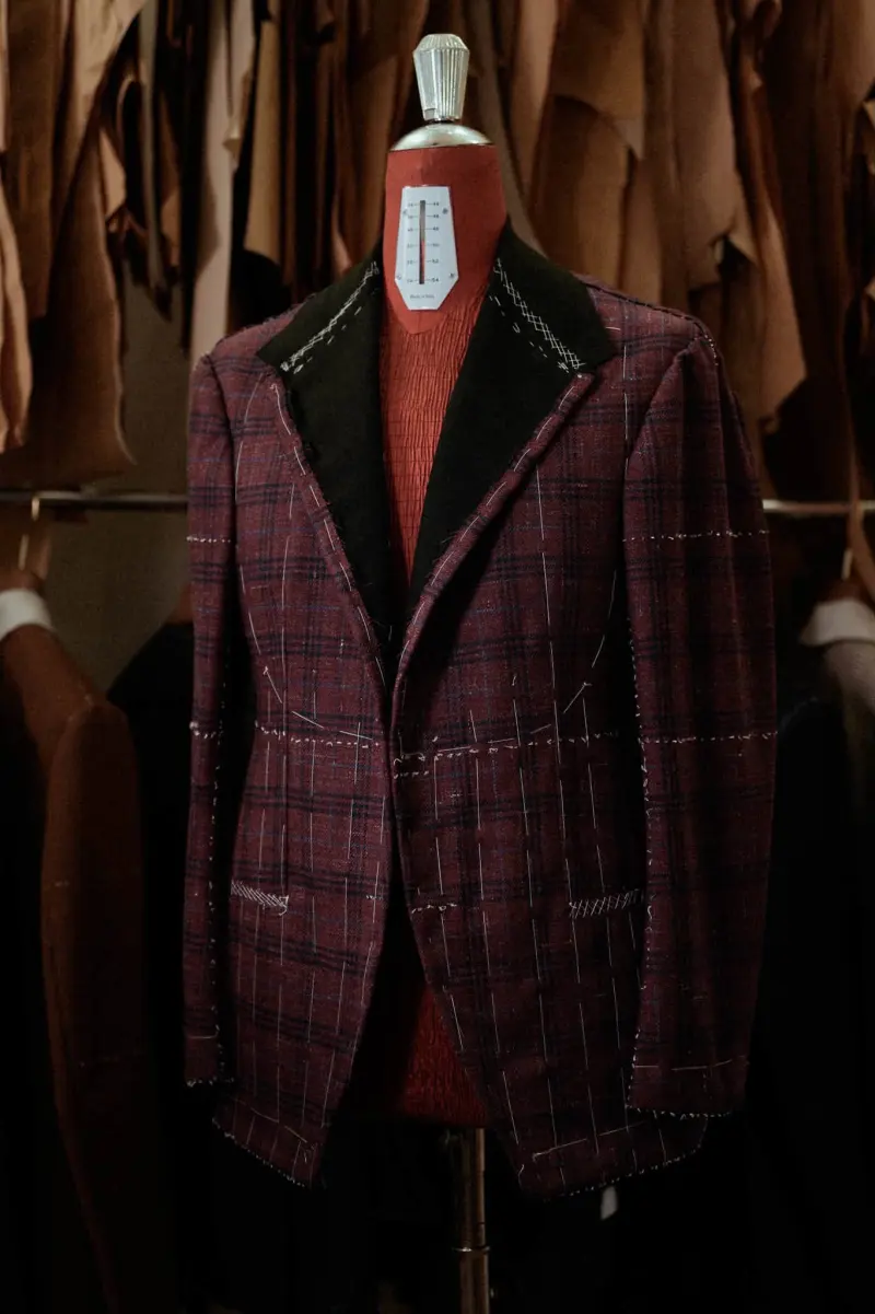 An unfinished red checked jacket on a mannequin in the atelier, with white threads and chalk marks