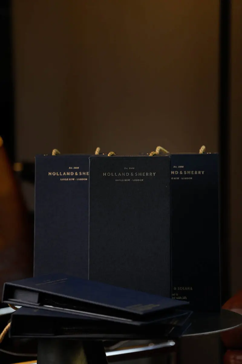 Three dark Holland & Sherry cloth boxes standing side by side in low light