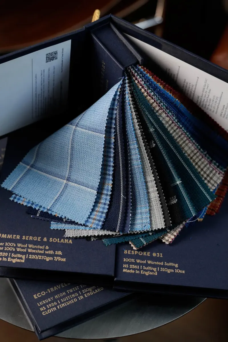 A fan of checked cloth swatches in blues and greens resting on a Holland & Sherry box