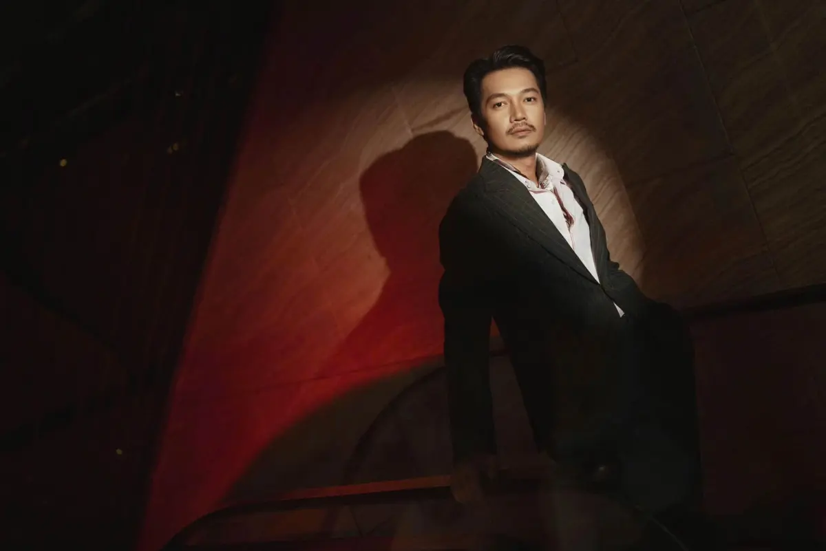 Quang Tuấn leaning on a railing, with red light falling behind him
