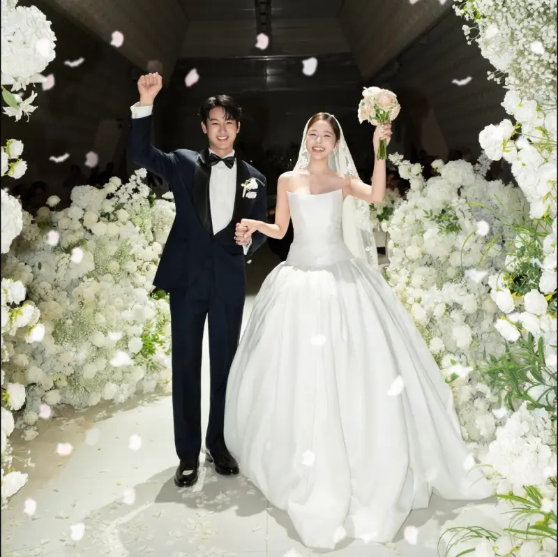 The groom and bride walking down a flower-lined aisle as petals fall