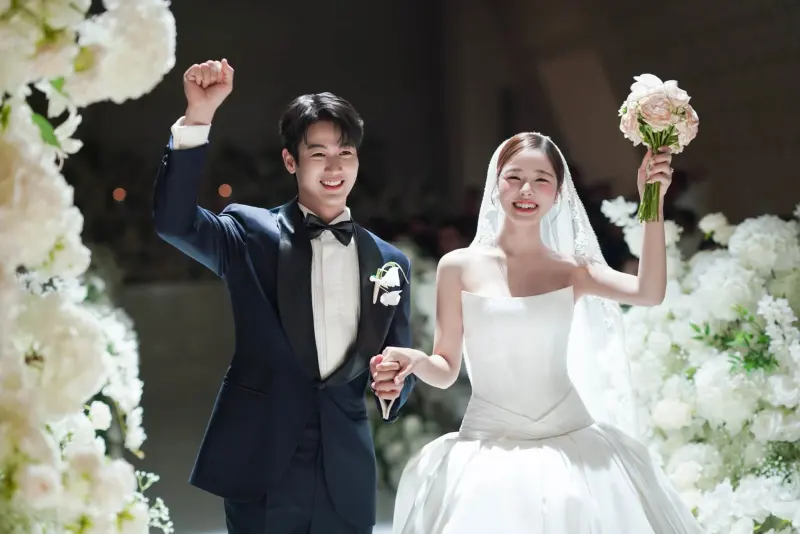 The groom in a tuxedo and the bride raising their hands in celebration