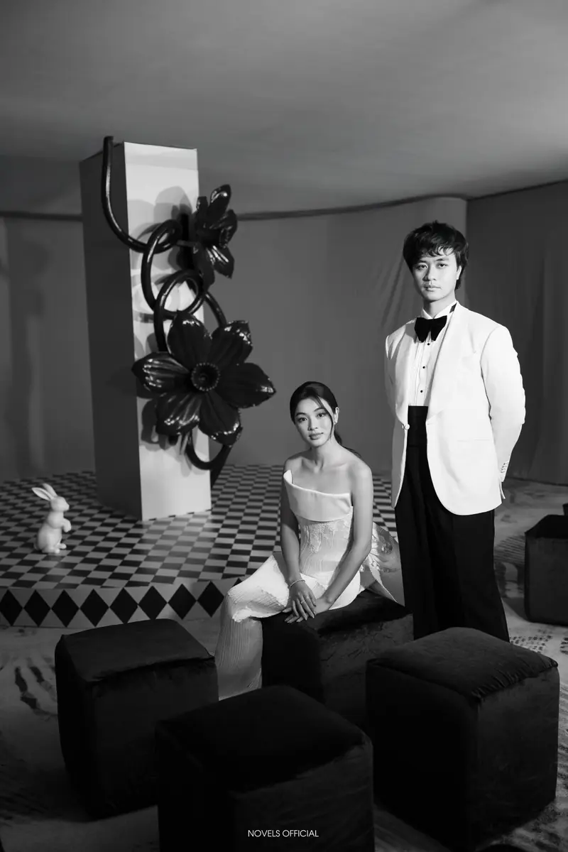 A man in a white dinner jacket and bow tie beside a woman in a white dress on a black-and-white studio set