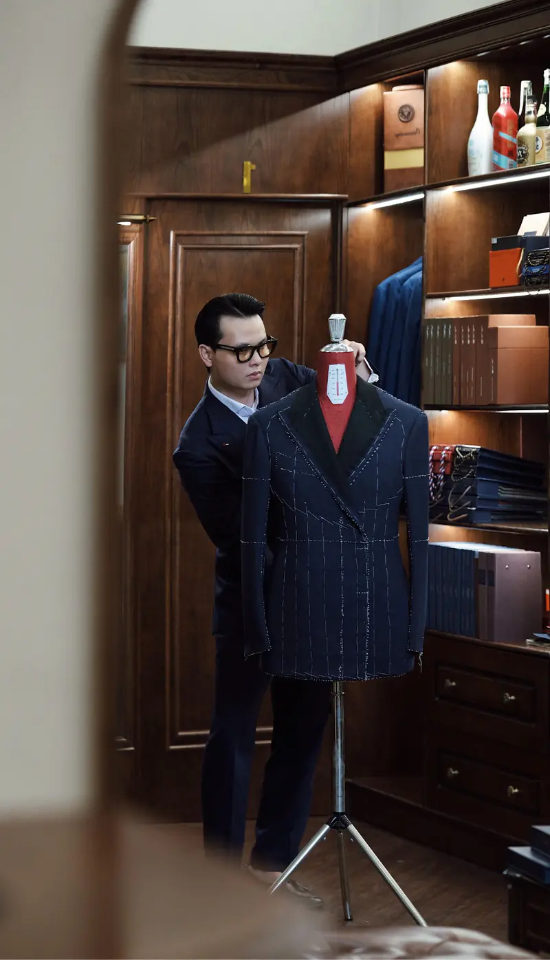 A tailor adjusting a navy double-breasted jacket on a dress form