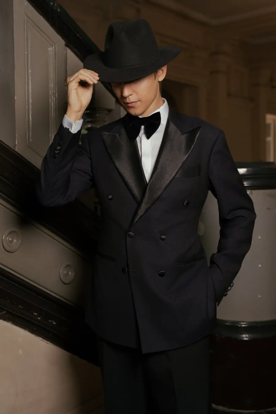 A man in a black double-breasted tuxedo with satin lapels, bow tie and fedora