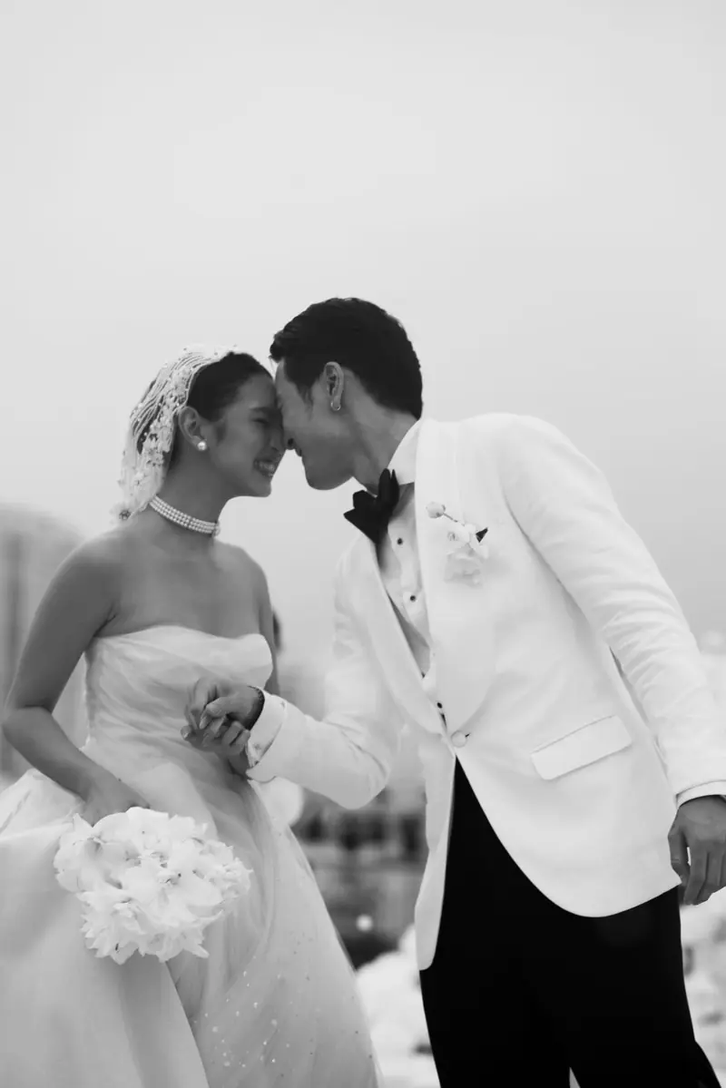 A groom in a white dinner jacket and black bow tie with his bride on their wedding day, in black and white