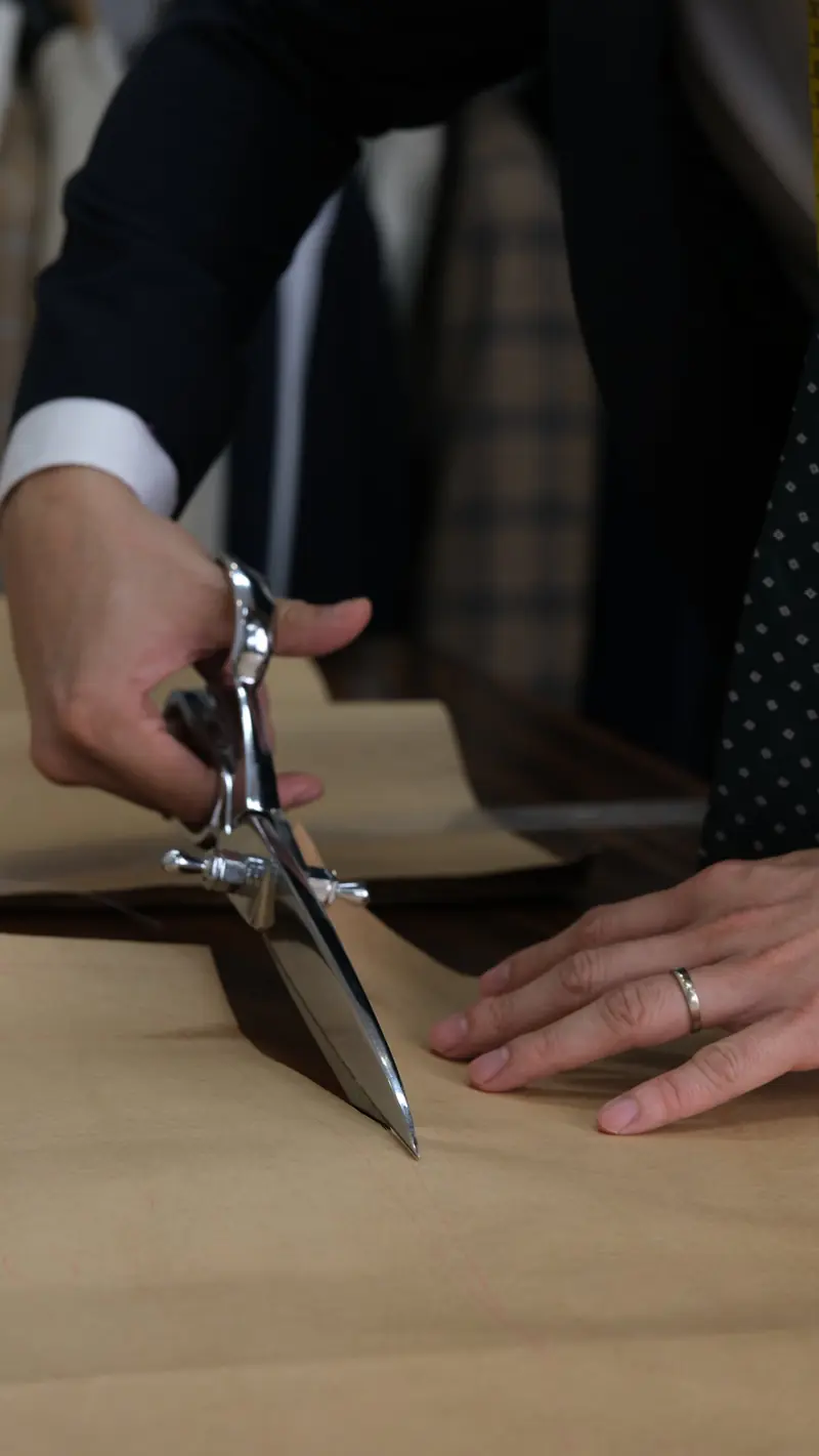Tailor cutting a brown paper pattern with shears on the cutting table