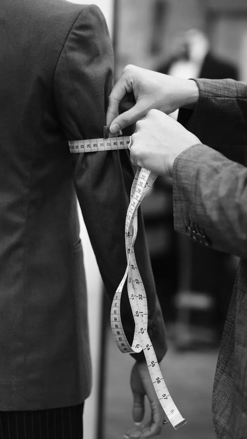 A tailor measuring a sleeve with a tape measure